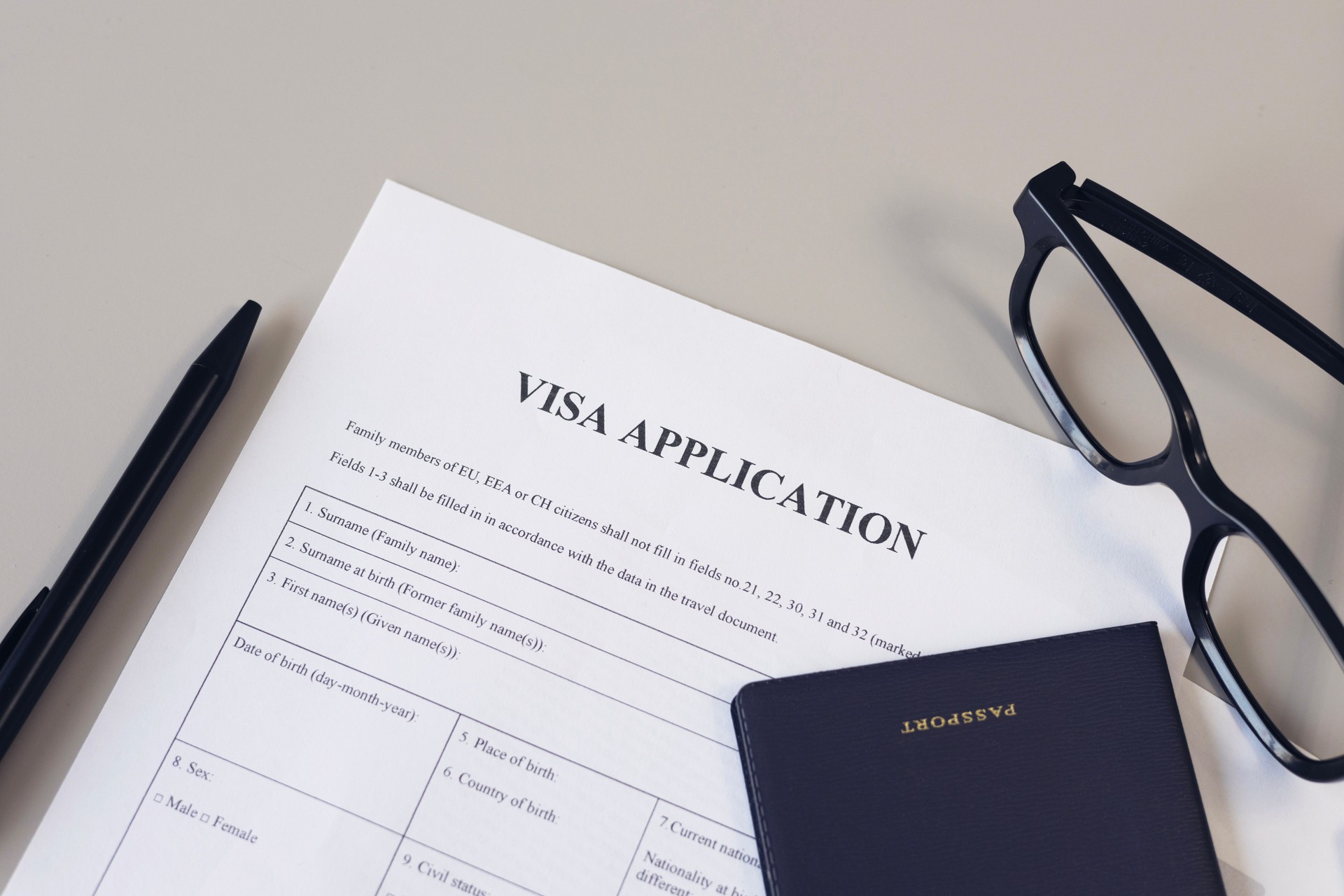 Visa application form, pen, eye glasses and passport on desk.